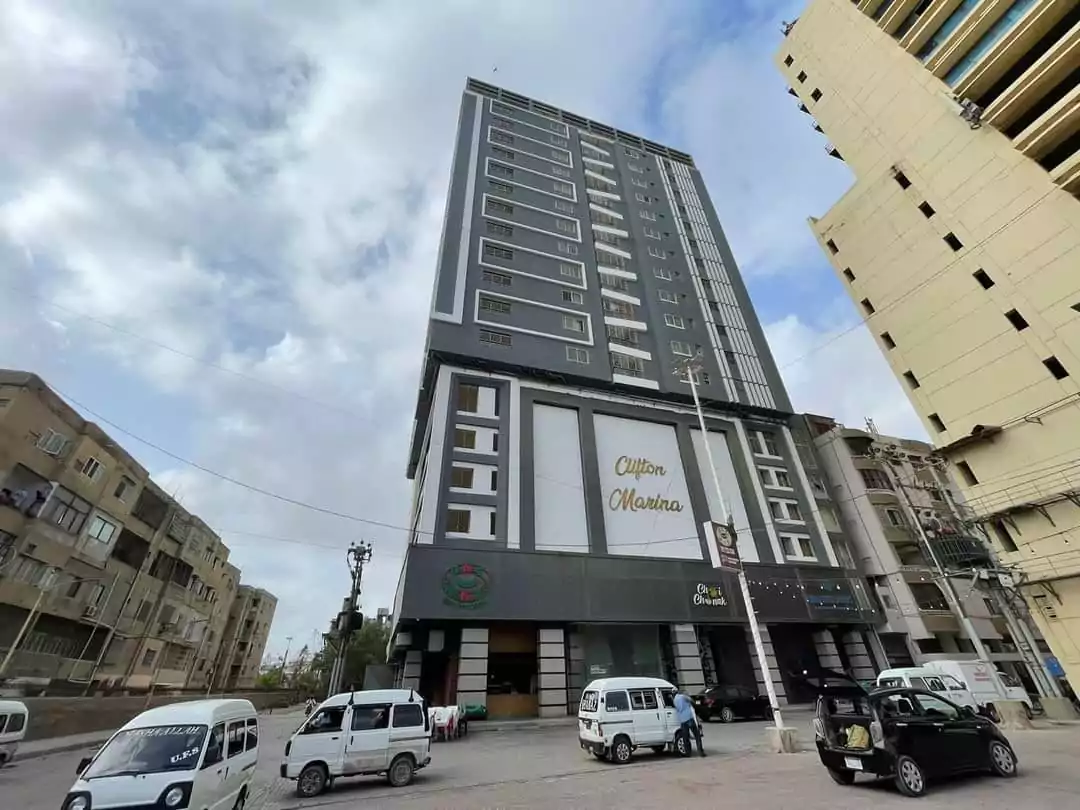 Modern multi-story Clifton Mansion building in Karachi with grey facade, balconies, prominent signage, street entrance and pa