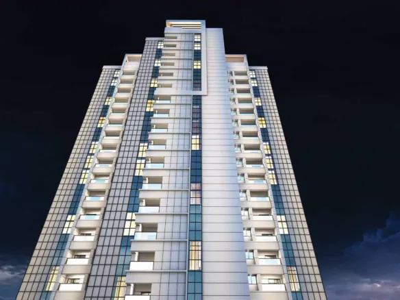 Night View Of Greens Three Clifton High-Rise Apartment Facade With Glass Panels, White Cladding, And Multiple Balconies