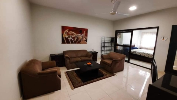 Living Room With Brown Leather L-Shaped Sofa, Armchairs, Coffee Table, Ceiling Fan, Wall Art, Sliding Glass Door To Bedroom I
