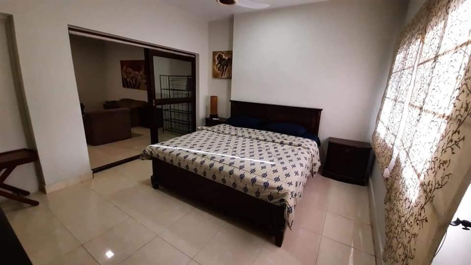 Fully Furnished Portion for Rent in DHA Phase 4, Karachi (2) Spacious bedroom with wooden king bed, blue bedding, nightstands, ceiling fan, sliding doors to living area in fully furnishe