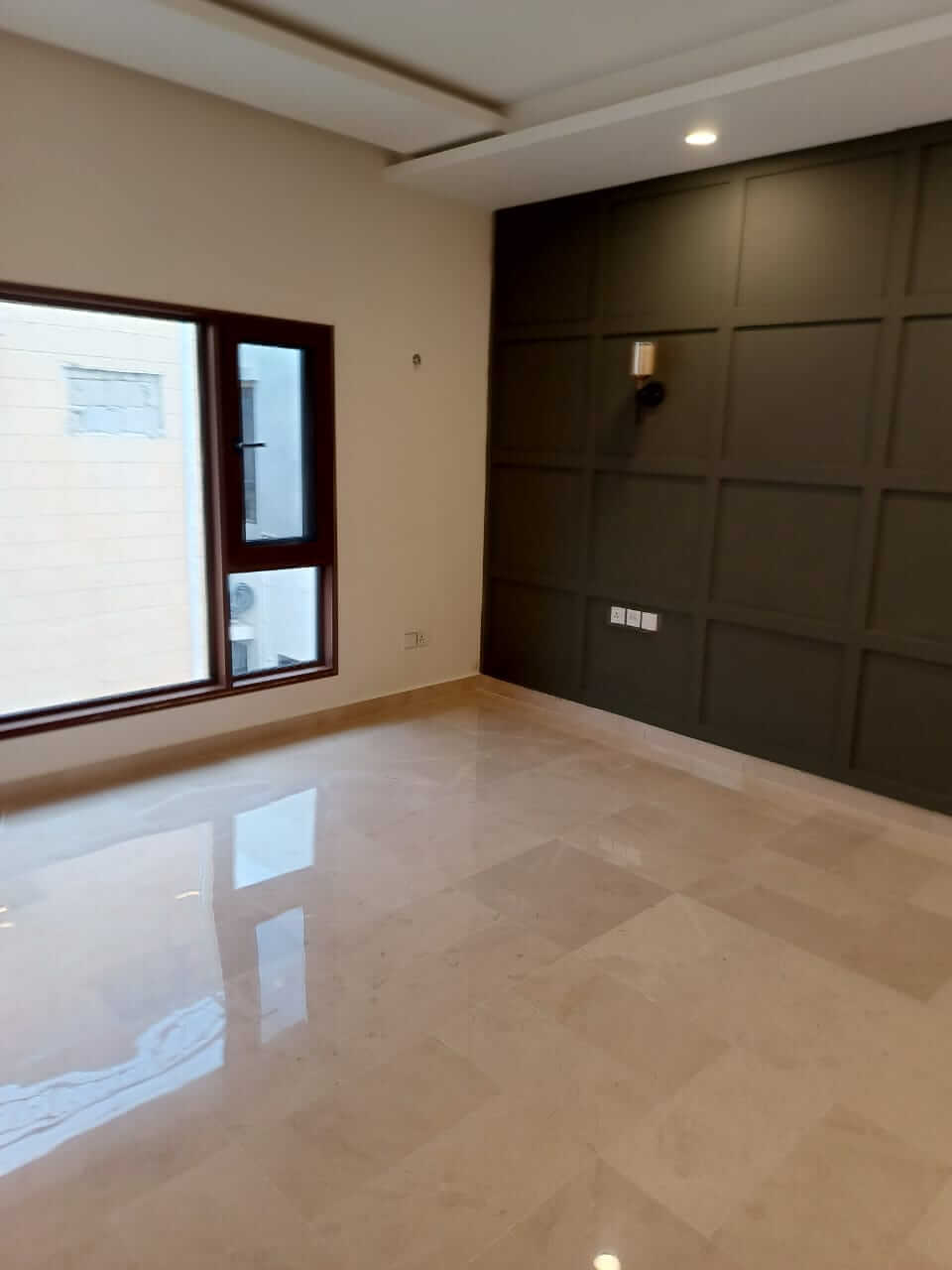 Brand New Stylish Bungalow For Rent in DHA Phase 4 Karachi (10) Spacious empty room with shiny beige tiled floor, large brown-framed window, dark paneled accent wall in brand new stylish bu