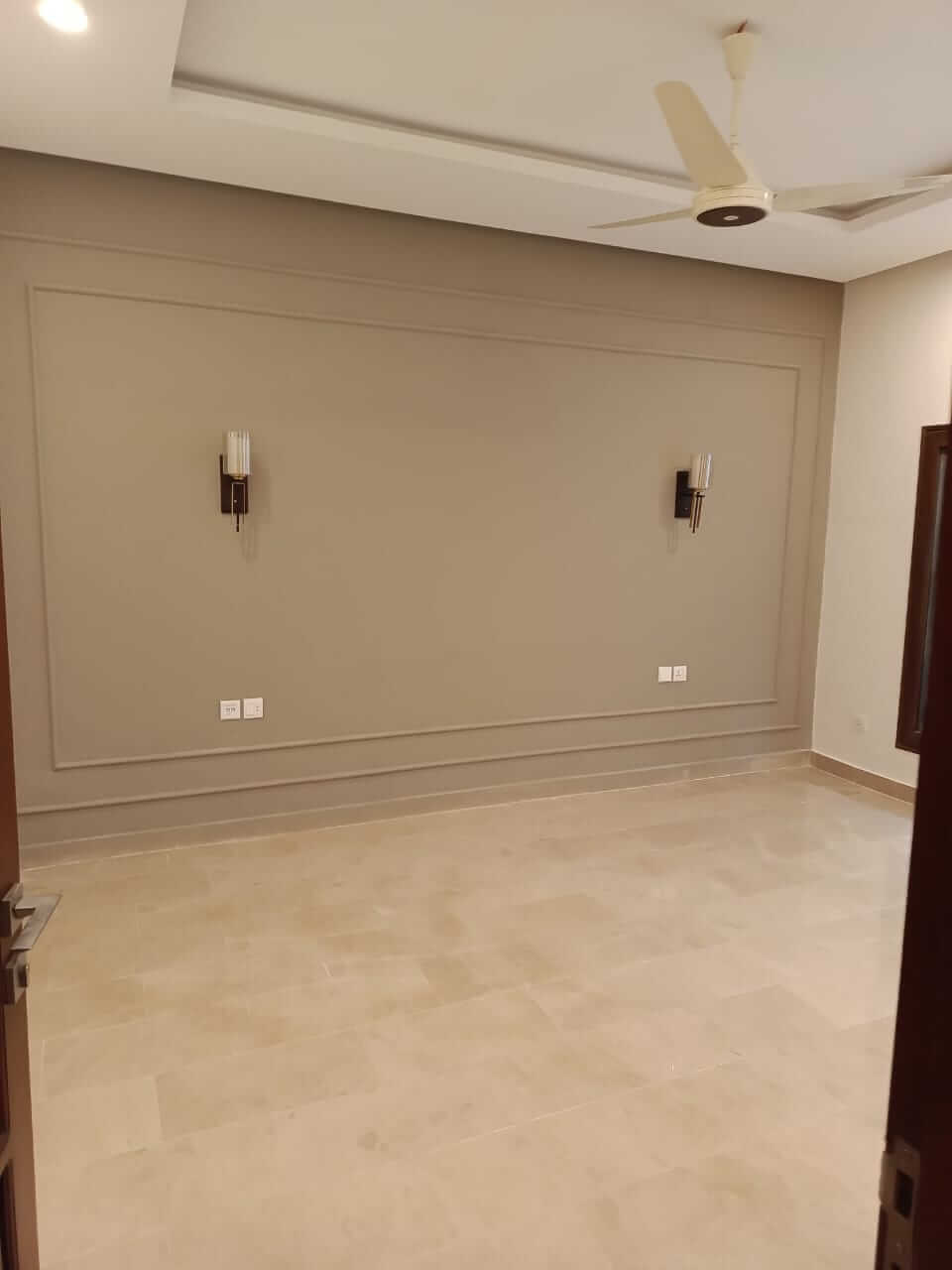 Brand New Stylish Bungalow For Rent in DHA Phase 4 Karachi (12) Spacious room with beige marble flooring, large feature wall, wall sconces, ceiling fan in brand new stylish bungalow for ren