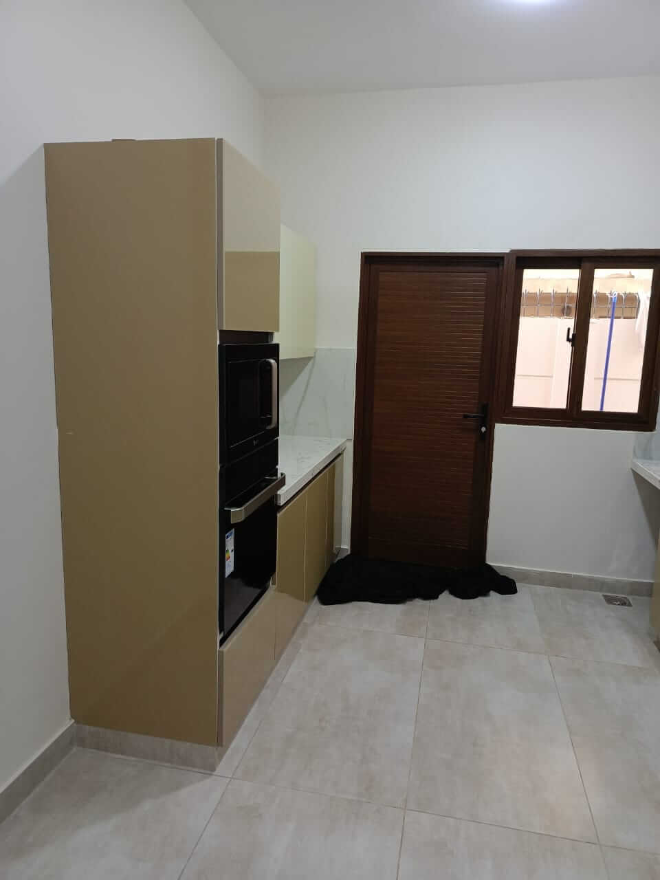 Brand New Stylish Bungalow For Rent in DHA Phase 4 Karachi (3) Modern kitchen with beige cabinets, built-in oven and microwave, wooden door, tiled floor in bungalow for rent DHA Phase 4 Ka