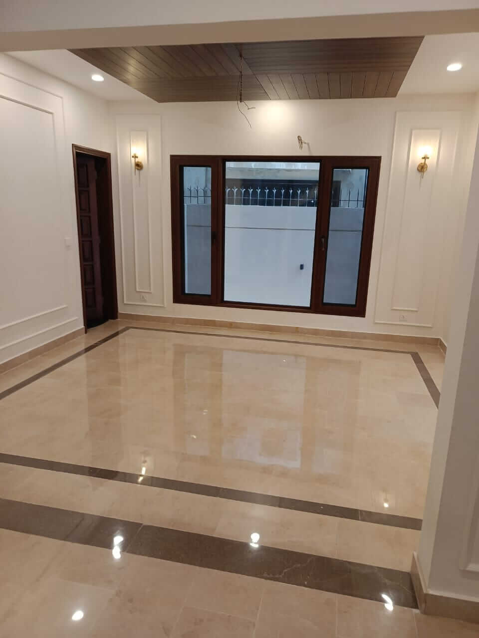 Brand New Stylish Bungalow For Rent in DHA Phase 4 Karachi (4) Spacious living area with polished marble flooring, wooden false ceiling, large windows and wall sconces in bungalow for rent