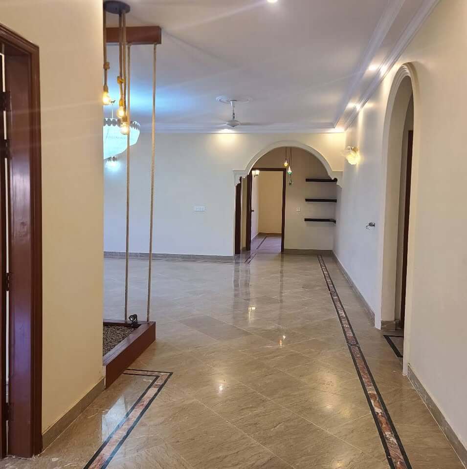 Supreme Luxury Bungalow for Sale in DHA Phase 6, Karachi (1) Spacious corridor in DHA Phase 6 bungalow with marble flooring, wooden doors, arched doorways, pendant lights, and shelves