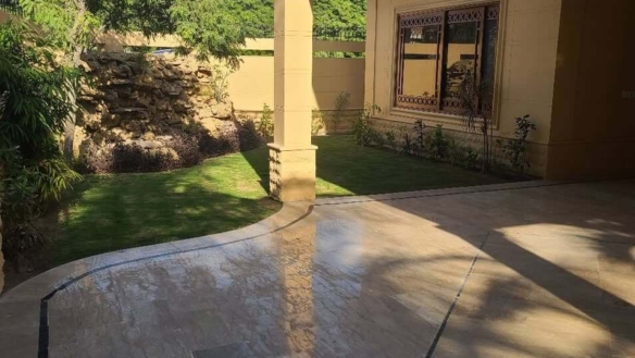 Luxury Bungalow Exterior In Dha Phase 6 With Beige Tiled Patio, Green Lawn, Rock Garden, Pillars, And Arched Windows