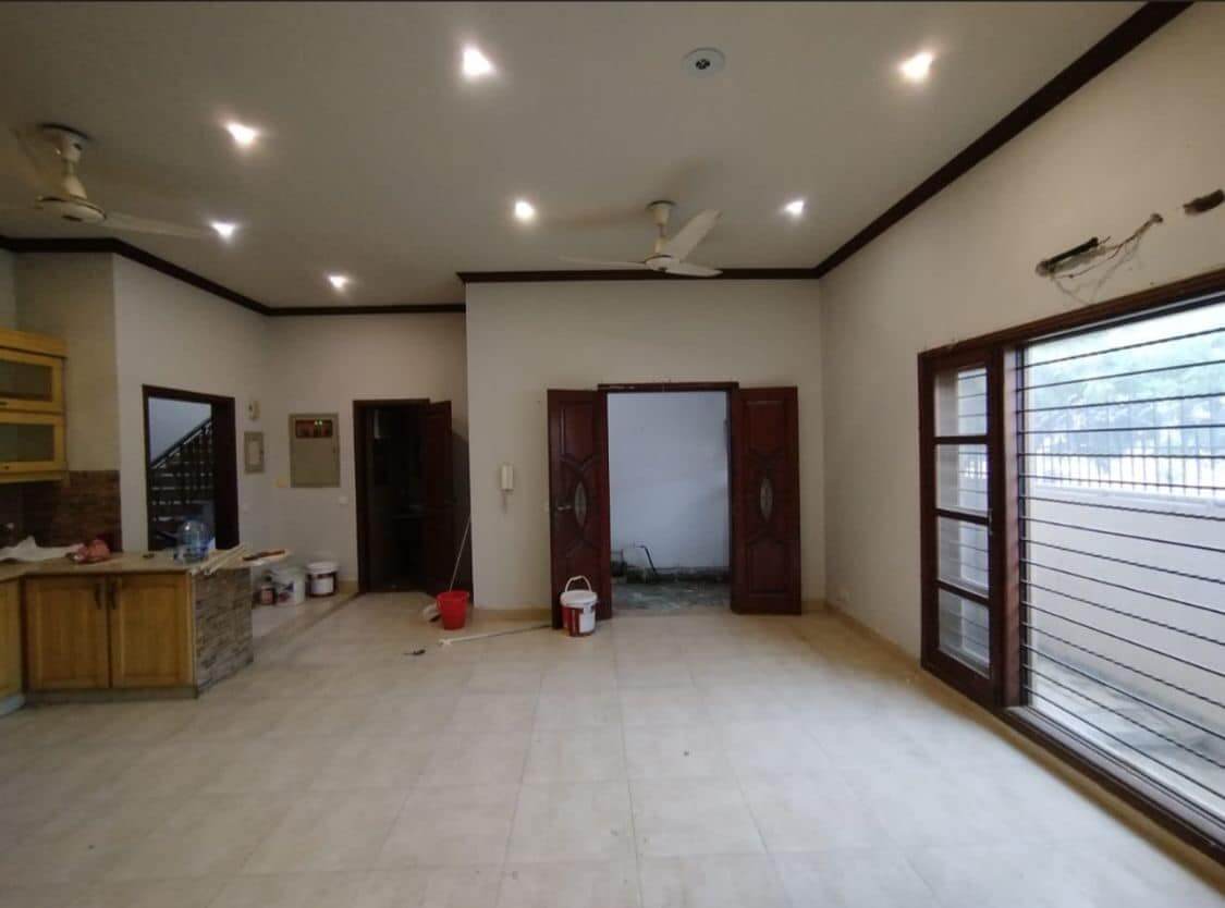 Supreme Luxurious House for Sale in DHA Phase 8, Karachi (1) Spacious open-plan living and kitchen area with ceiling fans, large grilled windows, wooden cabinets, tiled floors in DHA Pha