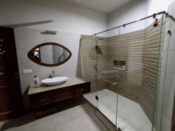 Modern bathroom with frameless glass shower, wooden vanity, oval sink, and beige tiled walls in luxurious house for sale in D