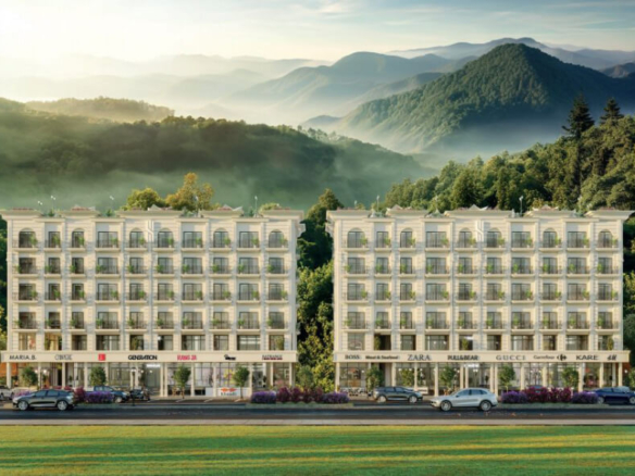 Twin modern apartment buildings in Sky Hills Islamabad with balconies, ground-floor shops, lush green lawns, and misty mounta