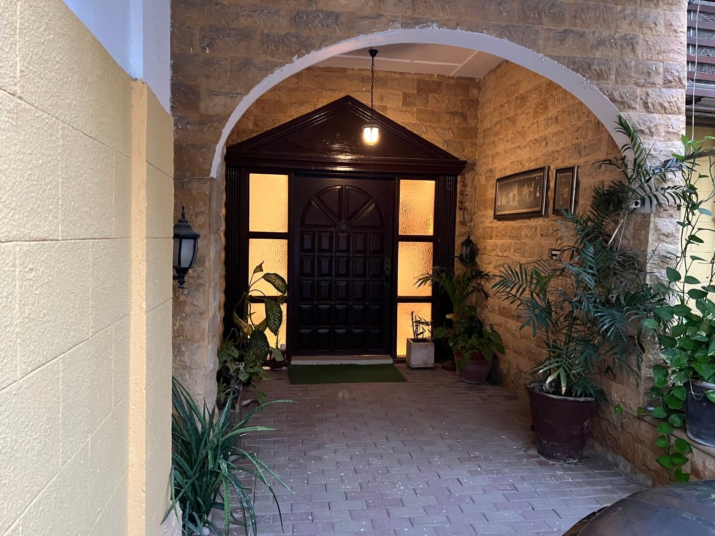 Portion for Rent in DHA Karachi – Fully Furnished Prime Location MaxX Capitals (13) Entrance of fully furnished portion for rent in DHA Karachi: stone archway, dark wooden door with glass panels, potted plants