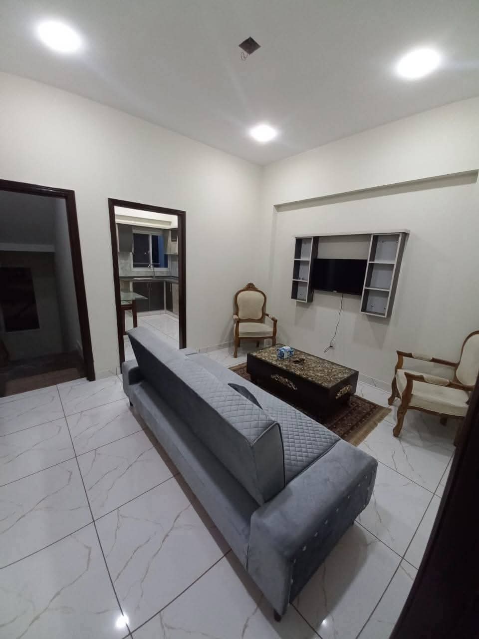 Fully Furnished Studio Apartment For Short & Long Term Rent – DHA Phase 6 MaxX Capitals (1) Living room in fully furnished studio apartment, DHA Phase 6 Karachi, with gray velvet sofa, armchairs, wooden coffee table,