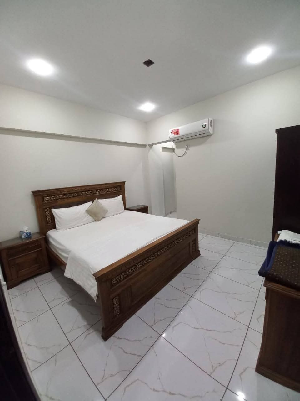 Fully Furnished Studio Apartment For Short & Long Term Rent – DHA Phase 6 MaxX Capitals (3) Carved wooden bed with white linens, matching nightstands and wardrobe in fully furnished studio apartment bedroom, DHA Phase