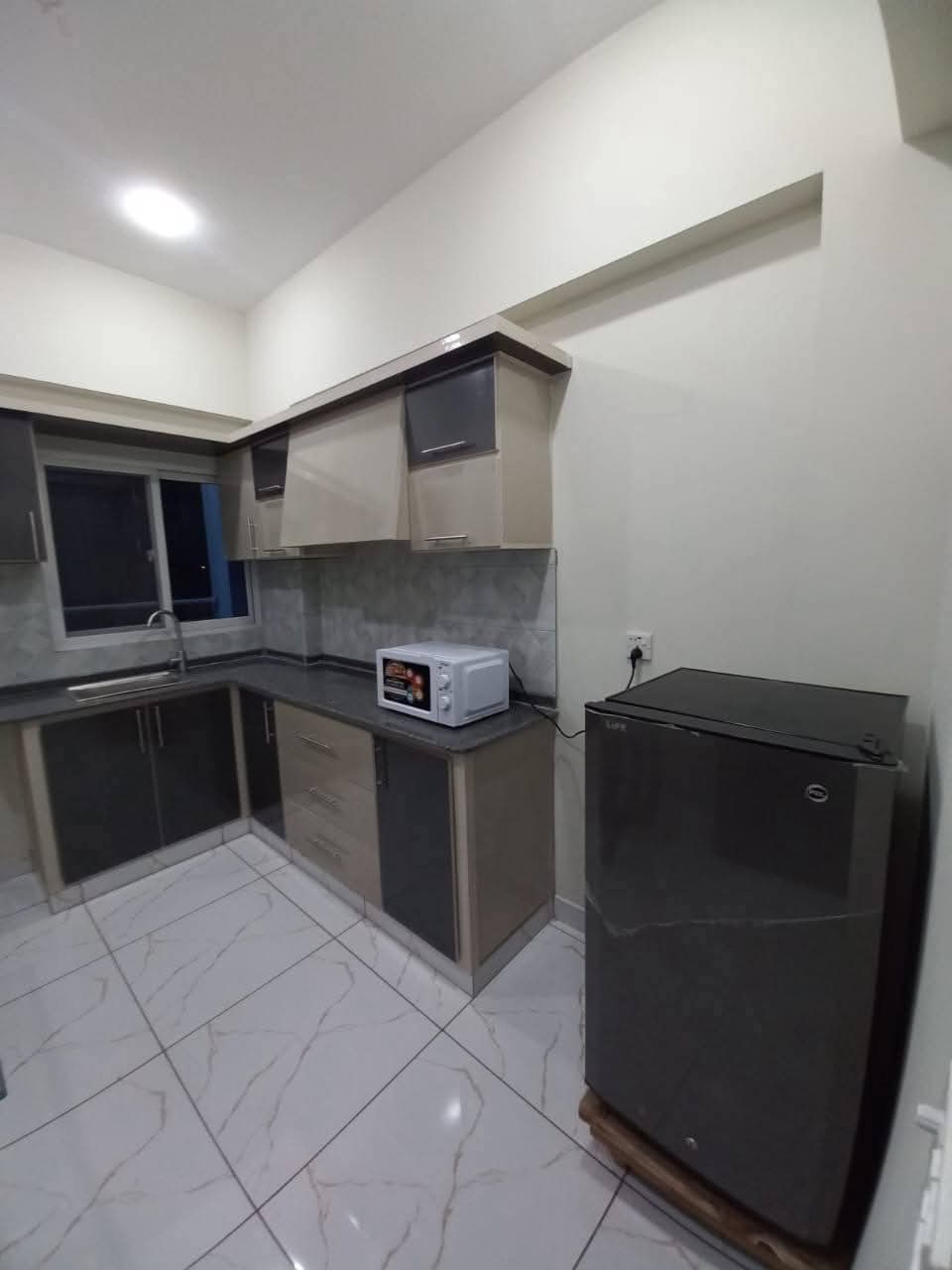 Fully Furnished Studio Apartment For Short & Long Term Rent – DHA Phase 6 MaxX Capitals (4) Compact kitchen in fully furnished studio apartment, DHA Phase 6, Karachi, with grey cabinets, sink, microwave, and mini frid