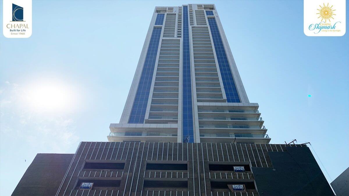 Chapal Skymark – 50-storey Luxury Residential Tower (1) Chapal Skymark 50-storey tower with white and blue striped facade, glass balconies, rising against blue sky and sun