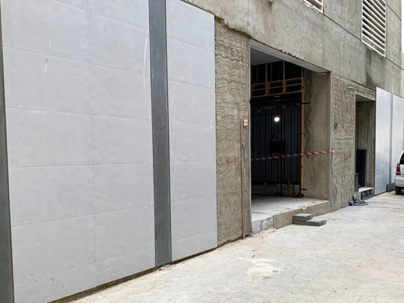 Chapal Skymark 50-storey tower construction: grey concrete walls with panels, open metal-framed doorways, parked silver car i