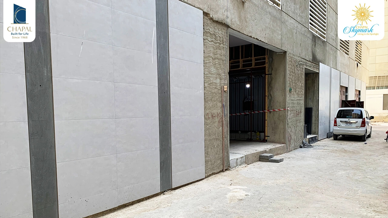 Chapal Skymark – 50-storey Luxury Residential Tower (2) Chapal Skymark 50-storey tower construction: grey concrete walls with panels, open metal-framed doorways, parked silver car i