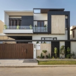 Maxx Capitals Modern Dha Phase 8 Karachi House Front Elevation With Balcony, Wooden Gate, And Landscaped Boundary